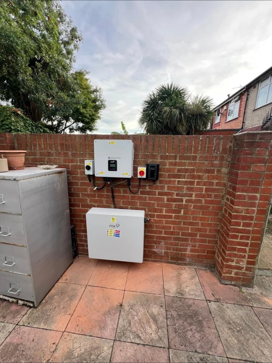 A Fox ESS battery and inverter installed on an exterior garden wall, with isolator switches mounted alongside.
