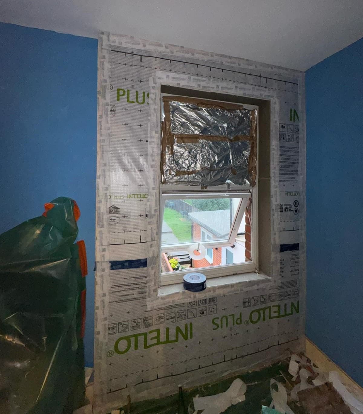 The same window reveal from a wider angle, showing the membrane lapped and taped across the full wall before the insulation boards go on.
